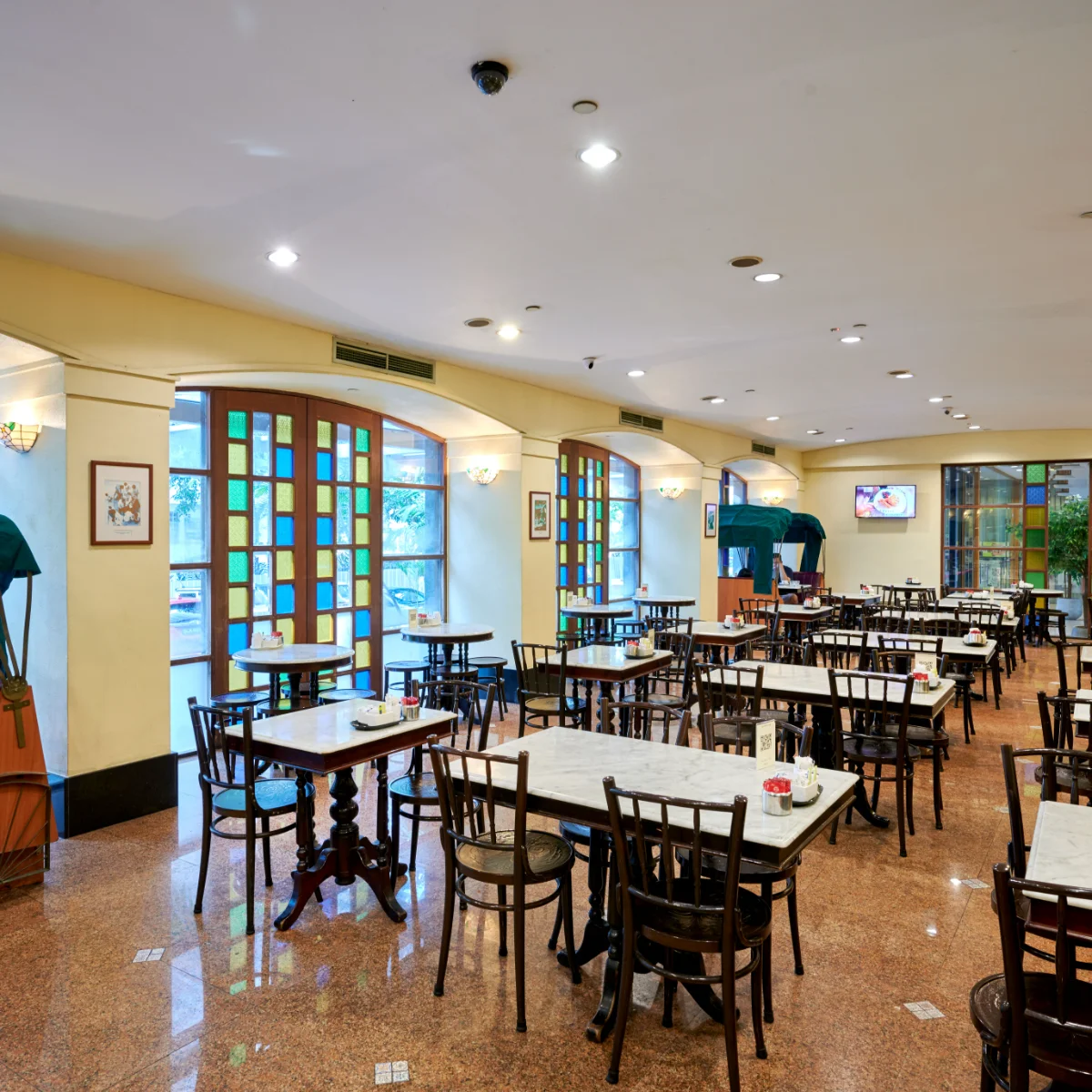 The coffeehouse on the ground floor of Hotel Royal, with marble tables and a trishaw bench by the window.