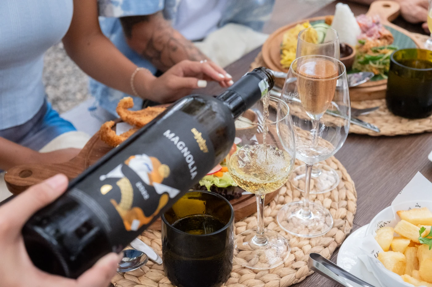 White wine being poured at a table laid with tasting glasses and shared plates.
